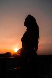 Silhouette woman standing against orange sky during sunset