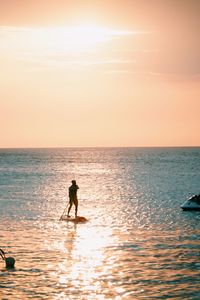 Silhouette woman standing in sea against sky during sunset