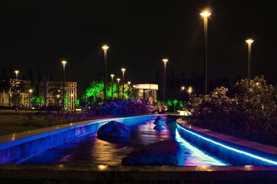 Illuminated street by swimming pool at night