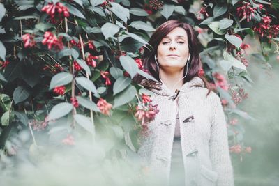 Portrait of young woman standing by flowering plants