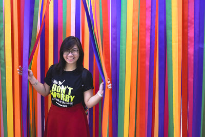 Portrait of smiling young woman standing against multi colored wall