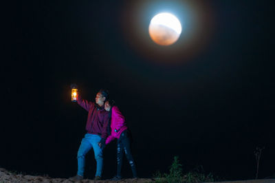 Rear view of couple standing against illuminated lights at night