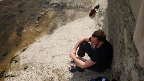 High angle view of young man sitting by rock