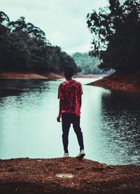 Rear view of man standing by lake against sky