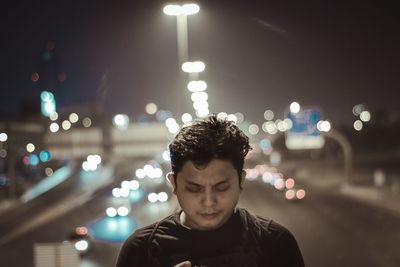 Portrait of young man standing on illuminated street at night