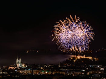 Firework display in city against sky at night