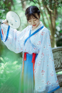 Woman in kimono holding hand fan outdoors