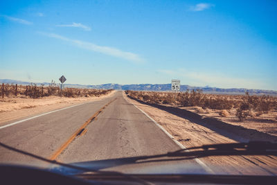 Road amidst fields against sky seen through car windshield