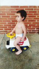 Cute boy playing with toy against brick wall