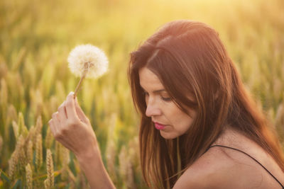 Close-up side view of woman holding dandelion flower during sunset