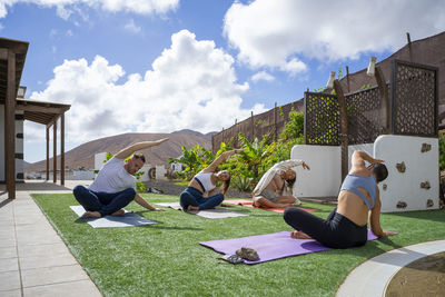 Yoga instructor and multiracial friends stretching on exercise mat in back yard