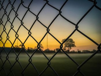 Close-up of chainlink fence against sky during sunset
