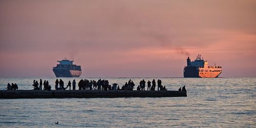 Silhouette people on ship in sea against sky during sunset