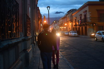 Rear view of couple walking on sidewalk in city at dusk