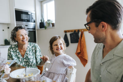 Cheerful daughter looking at father while sitting next to grandmother at home