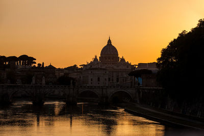 Arch bridge over river against buildings during sunset