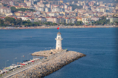 Lighthouse in sea against cityscape