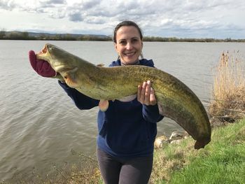 Portrait of smiling woman holding dead fish by lake