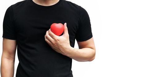 Midsection of man holding red heart model while standing against white background