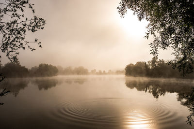 Scenic view of lake against sky with fog during sunset