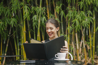 Young woman using phone while standing by plants