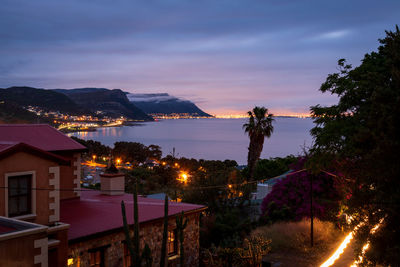 Illuminated buildings by sea against sky at night