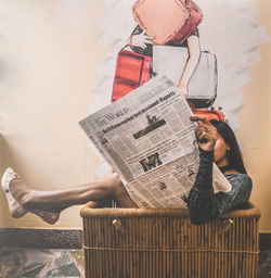 Woman reading newspaper while sitting in basket at home