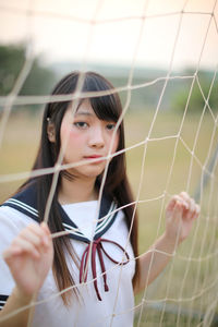 Portrait of young woman standing by sports net