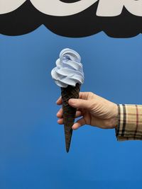 Low angle view of hand holding cross against clear blue sky