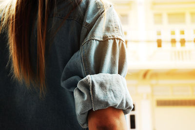 Midsection of woman wearing denim jacket standing against building