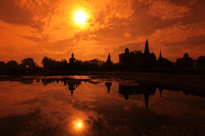 Silhouette buildings by lake against sky during sunset