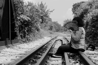 Side view of woman holding hand fan while sitting on railroad track