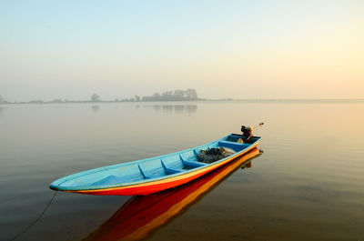 Kayak moored on lake against sky in foggy weather during sunset