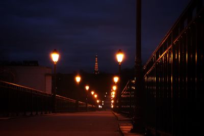 Illuminated street lights on bridge against sky at night