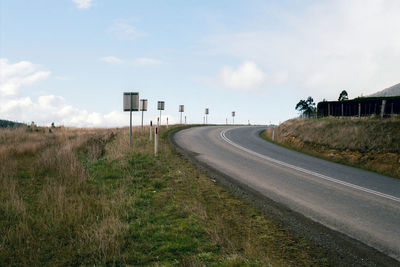 Empty road amidst field against sky