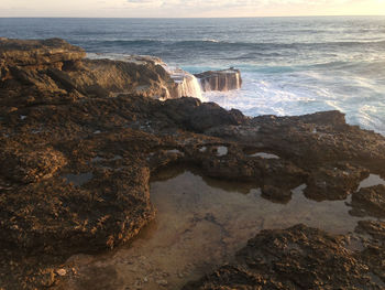 Scenic view of waves splashing on cliff during sunset