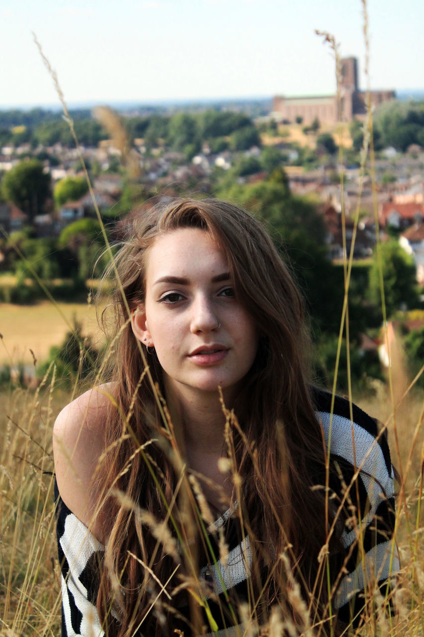 one person, portrait, young adult, young women, leisure activity, looking at camera, lifestyles, day, long hair, real people, focus on foreground, hair, nature, land, front view, field, beauty, hairstyle, outdoors, beautiful woman, contemplation, teenager