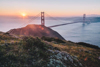 Suspension bridge over sea against sky during sunset