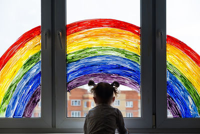 Little girl on background of painting rainbow on window. kids leisure at home. 