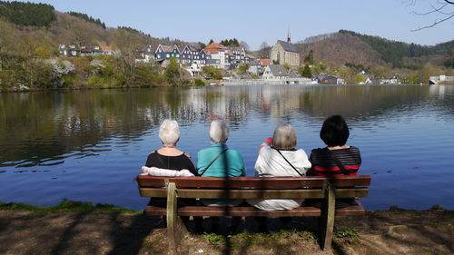 Rear view of women in bench overlooking calm lake