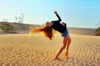 Full length of woman with arms raised on beach against sky