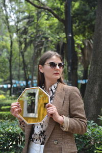 Young woman using mobile phone while standing on tree