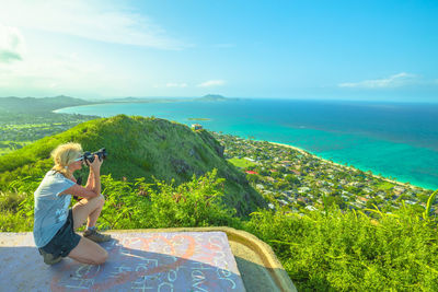 Side view of woman photographing while kneeling against sea