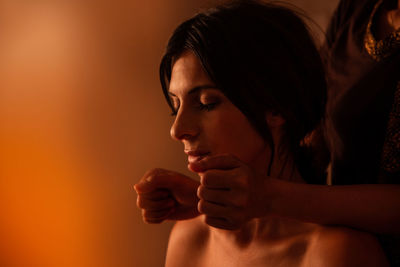 Asian female massagist in traditional clothes giving a thai massage to a caucasian woman sitting on a bed in a room lit with warm lights