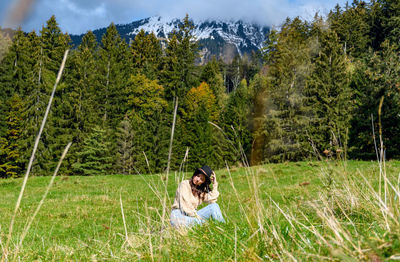 Young woman sitting in the middle of a green pasture in mountains.