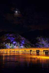 Illuminated bridge over river against sky at night