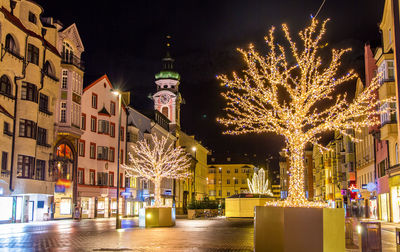 Illuminated christmas tree by buildings in city at night