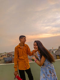 Happy friends standing against sky in city during sunset