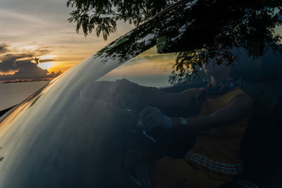 Rear view of woman sitting in car by sea against sky during sunset