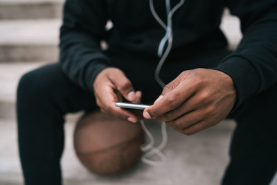 Midsection of man using mobile phone while sitting outdoors